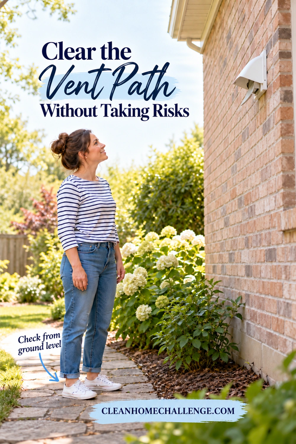 A woman stands on a level garden path and looks up at an exterior dryer exhaust hood on a brick wall.