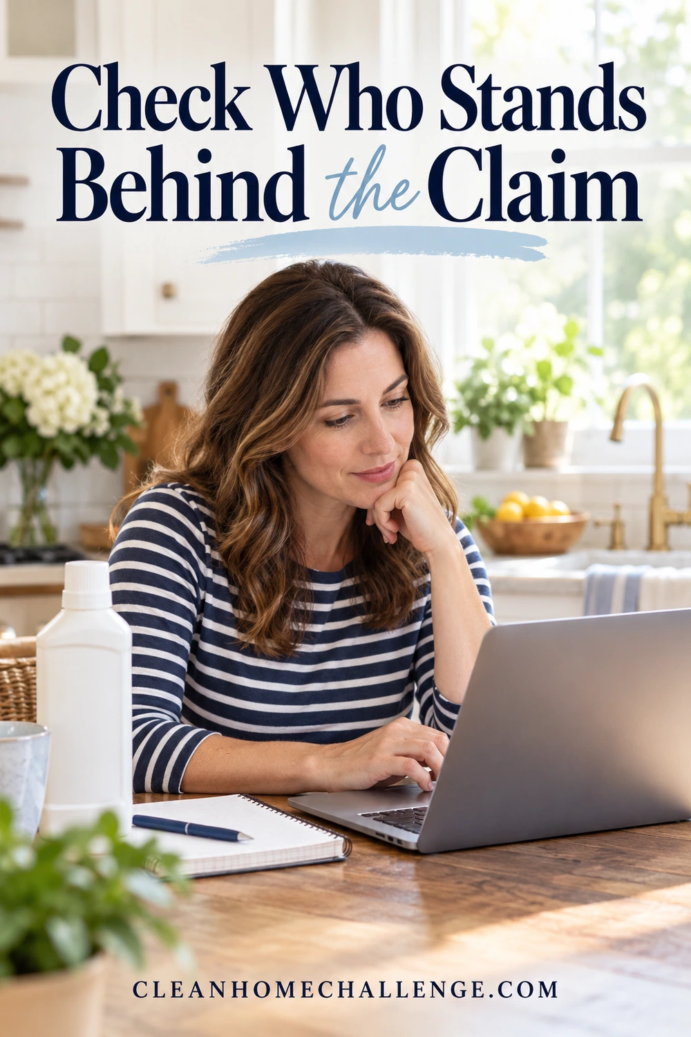 Woman at kitchen table uses laptop beside a capped white bottle and notebook.