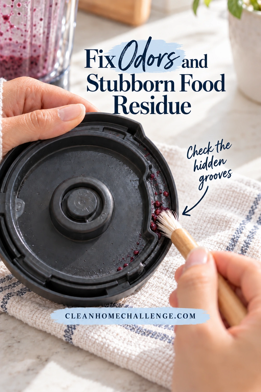 An adult holds a detached blender lid by its edge while a small soft brush cleans berry residue from an accessible underside groove.