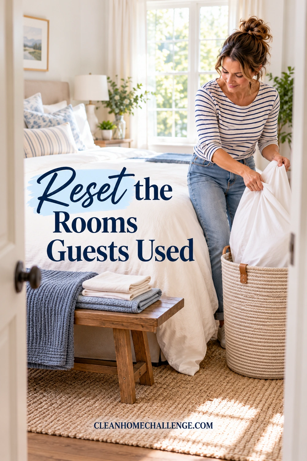 A woman puts used white bedding into a woven hamper beside a bed, with folded linens on a nearby bench.