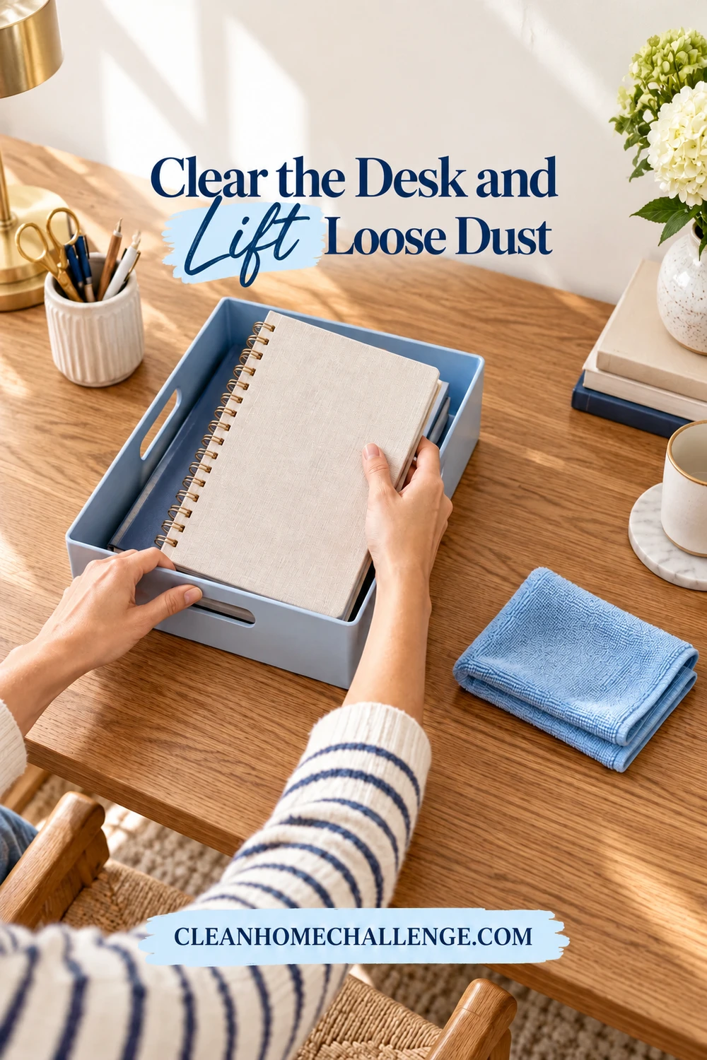 Two hands lift a closed notebook into a dry blue tray beside a folded dust cloth on an oak desk.